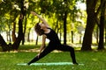 Woman practices yoga in morning in park in fresh air. Exalted Crescent Lunge pose