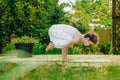 Woman practices yoga in summer garden: Kakasana, Crow Pose, with bent arms