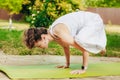 Woman practices yoga in summer garden: Kakasana, Crow Pose, with bent arms