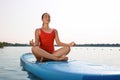 Woman practicing yoga on light blue SUP board on river Royalty Free Stock Photo