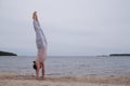 Woman practicing yoga doing handstand on beach outdoor.