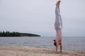 Woman practicing yoga doing handstand on beach outdoor.