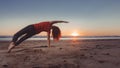 woman practicing yoga exercises while sun peeks over horizon of beach Royalty Free Stock Photo