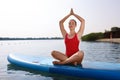 Woman practicing yoga on light blue SUP board on river Royalty Free Stock Photo