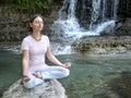 Woman is practicing yoga in lotus pose at mountain warefall lake Royalty Free Stock Photo