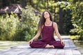 A woman practicing yoga, meditating with her eyes closed, sitting in a lotus position on a wooden bridge Royalty Free Stock Photo