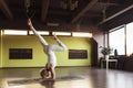 A woman practicing yoga performs shirshasana exercise with bent leg, inverted asana pose, standing on her forearms in the studio