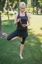 woman practicing yoga in tree pose and making sound with tibetan singing bowl