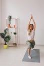 Woman practise yoga performs. Pose on mat inside of cozy room with plants and greenery. Healthy lifestyle concept.