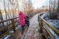 Woman with a pram walking along the walking path. First snow and footprints, wooden bridge, pole with lantern on sunny autumn day Royalty Free Stock Photo