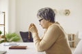 Senior woman who belongs to Catholic Christian Church sitting at desk and praying