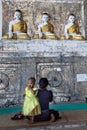 Woman praying to Buddha at a buddhist temple, barefoot. Child girl with thanaka paste on her face, used as cosmetic and mosquito