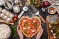 Woman preparing a festive dinner for two in honor of Valentine`s Day classic Italian pizza Margherita in the shape of a heart and