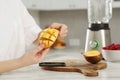 Woman preparing mango for tasty smoothie at white marble table in kitchen, closeup Royalty Free Stock Photo