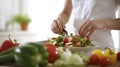 A woman preparing a salad, hands close-up, a cup of fresh salad, surrounded by vegetables, against the background of a Royalty Free Stock Photo