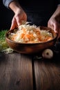 Woman preparing shredded cabbage and carrots to marinate, on dark wooden kitchen table. Generative AI