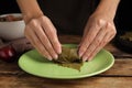 Woman preparing stuffed grape leaves at wooden table, closeup