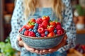 Woman presenting a bowl of mixed berries in a kitchen