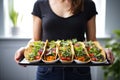 woman presenting multiple vegan tacos in a tray