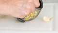 A woman presses fresh garlic using a garlic press tool on white cutting board on the kitchen table Royalty Free Stock Photo