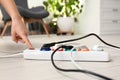 Woman pressing power button of extension cord on floor indoors. Electrician`s professional equipment