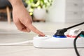 Woman pressing power button of extension cord on floor indoors. Electrician`s professional equipment Royalty Free Stock Photo