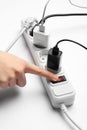 Woman pressing power button of extension cord on white background, closeup. Electrician`s