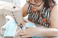 Mature woman produces homemade surgical masks - portrait of a senior woman who manufactures protective equipment during the