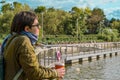 Woman in profile with cup of coffee stands on the pier of city pond and looks at the water Royalty Free Stock Photo