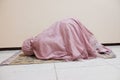 A woman is prostrating for prayer using a pink mukena