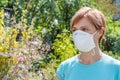 Woman in protection mask holding bouquet of wildflowers and trying to fight allergies