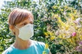 Woman in protection mask holding bouquet of wildflowers and trying to fight allergies