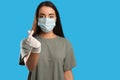 Woman in protective face mask and medical gloves showing heart gesture against blue background, focus on hand. Space for text Royalty Free Stock Photo
