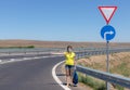 Woman in a protective mask and a backpack in hand hitchhikes on the road on a sunny summer day. Royalty Free Stock Photo