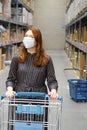 A woman in a protective mask with a cart in a supermarket. A girl in a store warehouse during a coronavirus epidemic, concept