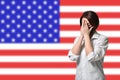 A woman in a protective mask covers her face with her hands against the background of the American flag. Concept of Royalty Free Stock Photo