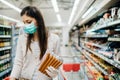 Woman with protective mask and gloves shopping for supply.Budget shopping at a supermarket.Buying processed nonperishable food.