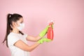 Woman in protective mask and green gloves holding chemical spray bottle on pink background. Cleaning products concept Royalty Free Stock Photo