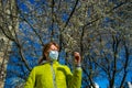 The woman in the protective mask in a park near the blossoming, magnolia tree wants to smell flowers on a sunny spring day