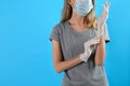 Woman in protective mask putting on medical gloves against light blue background, closeup. Space for text Royalty Free Stock Photo