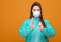 woman in protective medical equipment with antiseptic in hands medical mask on face on yellow background, coronavirus pandemic