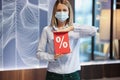 Woman in protective medical mask holding red sign with discount percentages in store