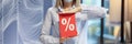 Woman in protective medical mask holding red sign with discount percentages in store