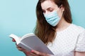 A woman in a protective medical mask is reading a book. Stay home