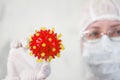 Woman in protective suit holds coronovirus model.