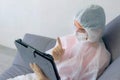 Woman in protective suit, mask, glasses, gloves talking video chat on tablet.