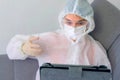 Woman in protective suit, mask, glasses, gloves talking video chat on tablet.