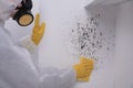 Woman in protective suit and rubber gloves removing mold from wall with rag, closeup