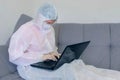 Woman in protective suit is typing on computer on quarantine.