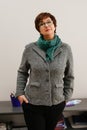 Woman / psychologist standing at the table wearing grey coat, black glasses green neckerchief